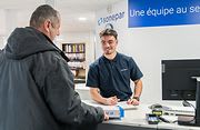 Employé de Sonepar souriant et discutant avec une cliente dans un magasin Sonepar, entourés de produits en rayons