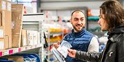 Employé de Sonepar souriant et discutant avec une cliente dans un magasin Sonepar, entourés de produits en rayons